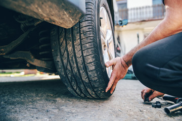 Close up of auto mechanic changing tire while crouching at workshop.