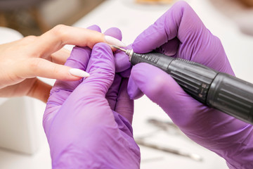 Manicurist work on a woman client hands, make her nails look beautiful. Salon procedure in process. Professional works in gloves using drill for sterility