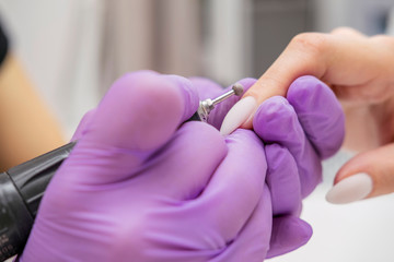 Manicurist work on a woman client hands, make her nails look beautiful. Salon procedure in process. Professional works in gloves using drill for sterility