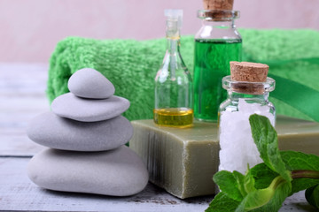 Fototapeta na wymiar Spa set: massage stones, aromatic oil, sea salt, green gel, organic soap and green towel on white wooden table