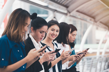Obraz na płótnie Canvas attractive asian businesswomen team playing smartphone outdoor city background