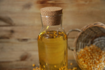 Fototapeta na wymiar corn oil in a bottle close-up with a basket of corn kernels scattered on a wooden rustic background