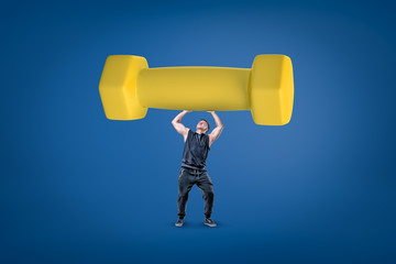 Strong muscular young man holding a big yellow dumbbell on blue background