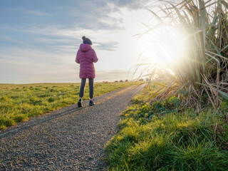 Girl walking by a path at sunset, autumn or fall season.Sunny evening, Sun flare, Girl dresses in a warm fall clothes.