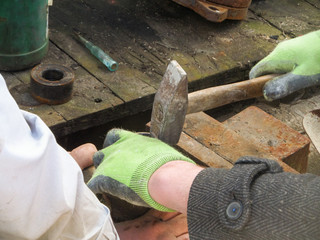 Hands worker in protective green gloves work with a hammer.