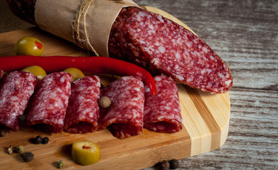 Italian salami with olives and spices on wooden background