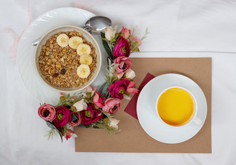 Obraz na płótnie Canvas Breakfast in bed with muesli, fruit and orange juice with flowers and a card
