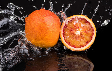 Fototapeta na wymiar Bloody orange whole and halves, slices with reflection on white and black background in a spray of water