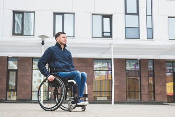 Young man in a wheelchair against the backdrop of a modern high-rise building.