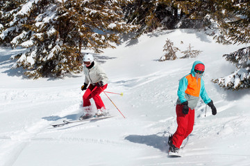 Skiers and snowboarders riding on a ski resort on snowy winter mountain with fir-tree background scenic view. Blue sky