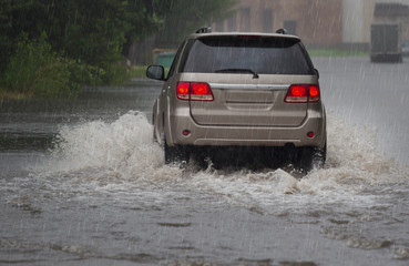 Obraz na płótnie Canvas Red car rides in heavy rain on a flooded road