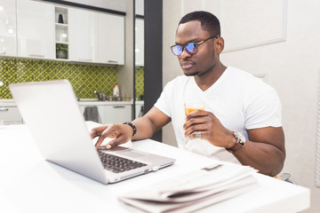 Fototapeta na wymiar Young African American businessman working on a laptop in the kitchen in a modern interior.