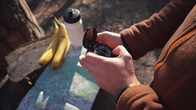 theme hiking and nature travel. Hands Caucasian male tourist break felled tree, stump in forest autumn sunny weather. Searching direction with compass on map. Theme navigation and plot route