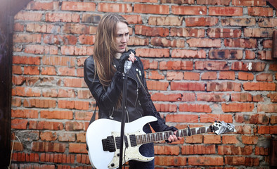 Beautiful young girl rocker with electric guitar. A rock musician girl in a leather jacket with a guitar sings. A rock band soloist plays the guitar and screams into the microphone.