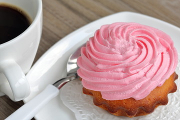 Cream cake and cup of coffee. Cake lies on a saucer. Near a coffee spoon.