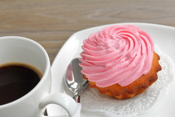 Cream cake and cup of coffee. Cake lies on a saucer. Near a coffee spoon.