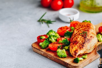 Grilled chicken breast with broccoli and  tomatoes on wooden cutting board