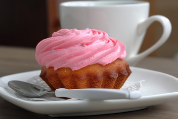 Cream cake and cup of coffee. Cake lies on a saucer. Near a coffee spoon.