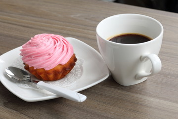 Cream cake and cup of coffee. Cake lies on a saucer. Near a coffee spoon.