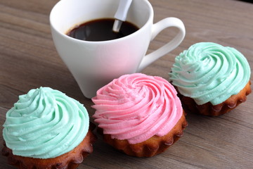Three cream cakes of different colors and a cup of coffee. A coffee spoon is dropped into the coffee cup.