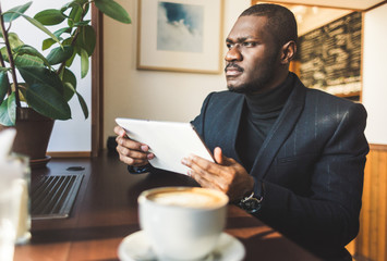 Young handsome dark-skinned businessman with tablet in cafe with a cup of coffee.