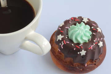 Chocolate coated cake with decorative topping. Nearby is a cup of coffee.