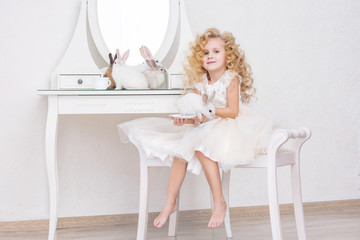 Fototapeta na wymiar Little beautiful and cute girl child in a fashionable festive dress and with animals rabbits in the mirror in a white interior
