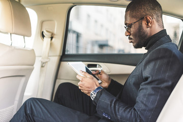 Young businessman using tablet while sitting in the backseat of a car.