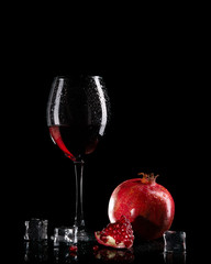 Pomegranate juice in a glass on a black background. Pomegranate fruit, ice cubes and a glass with fresh juice.
