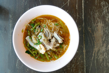 Spicy seafood noodles soup with pork bone crayfish, shrimp.  Asia food in pink bowl on wooden table background. Thai style noodle and street food of Thailand.   top view