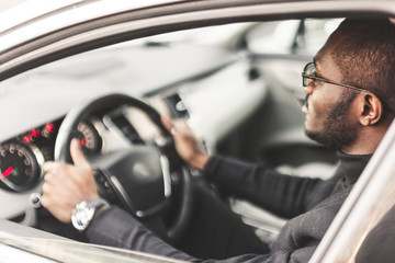 A young businessman in a suit sits at the wheel of a expensive car.