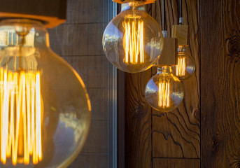 hanging retro spherical edison incandescent bulbs against a brown wall with a wooden texture and blurred foreground