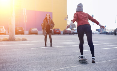 A young hipster girl is riding a skateboard. Girls girlfriends for a walk in the city with a skateboard. Spring sports on the street with a skateboard.
