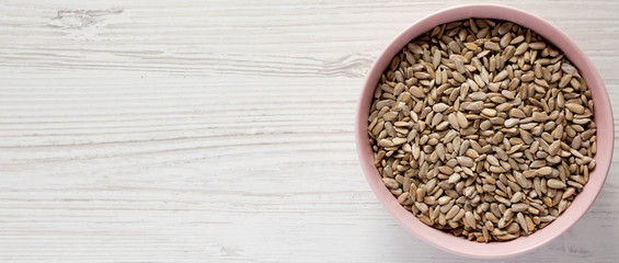 Рulled sunflower seeds in a pink bowl over white wooden background. Flat lay, top view, from above. Space for text.