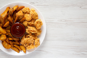 Fried potato wedges, chicken bites on a white plate over white wooden background. Flat lay, overhead, top view. Blank space.