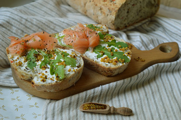 Sandwiches on two pieces of rye bread with cream cheese, arugula, mustard seeds and salmon on the wooden board. Concept of healthy trendy food. Delicious breakfast.