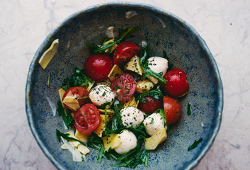 Healthy homemade vegetable salad with arugula, cherry tomatoes, artichoke and mozzarella cheese in bowl top view space for text