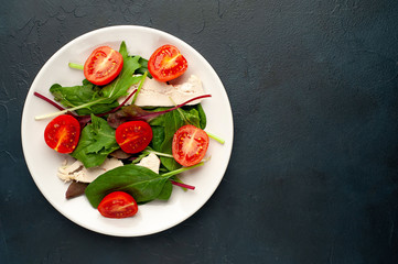 Mix fresh leaves of arugula, lettuce, spinach, tomato and chicken fillet for salad, on a white plate on a stone background with copy space for your text