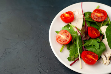 Mix fresh leaves of arugula, lettuce, spinach, tomato and chicken fillet for salad, on a white plate on a stone background with copy space for your text