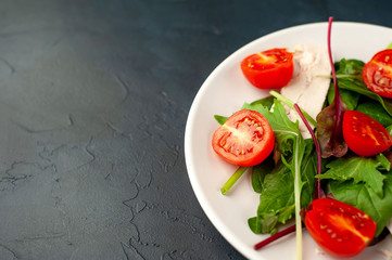 Mix fresh leaves of arugula, lettuce, spinach, tomato and chicken fillet for salad, on a white plate on a stone background with copy space for your text