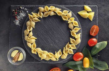 Pasta shells on black stone. Tomatoes and bay leaves with allspice and sea salt.