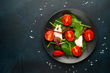 Mix fresh leaves of arugula, lettuce, spinach, tomatoes and chicken fillet for salad, on a dark plate against a background of concrete