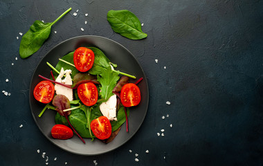 Mix fresh leaves of arugula, lettuce, spinach, tomatoes and chicken fillet for salad, on a dark plate against a background of concrete