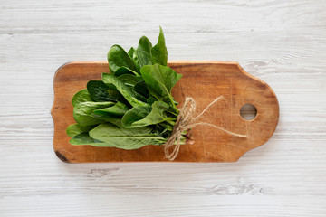 Fresh raw spinach on a rustic wooden board on a white wooden background. Flat lay, overhead, from...