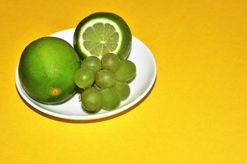 Saucer with two lemons and a bunch of grapes on a yellow background