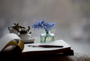Still life with vintage inkpot, notepad and blue spring flowers against the window