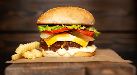  Delicious homemade hamburger made of beef, salad, cheese, cucumber and french fries on a wood background