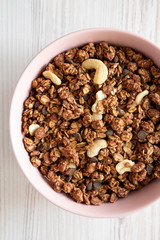 Homemade chocolate granola with nuts in a pink bowl over white wooden background, top view. From above, overhead, flat lay. Close-up.