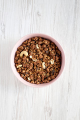 Homemade chocolate granola with nuts in a pink bowl over white wooden background, top view. From above, overhead, flat lay.
