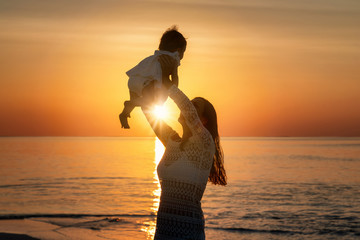 Mutter und Tochter spielen glücklich am Strand während eins Sonnenunterganges